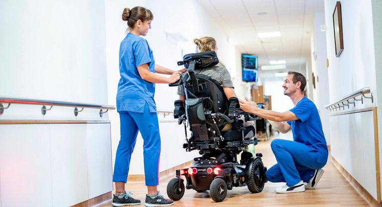 Zwei Pflegekräfte kümmern sich um einen Patienten im Rollstuhl