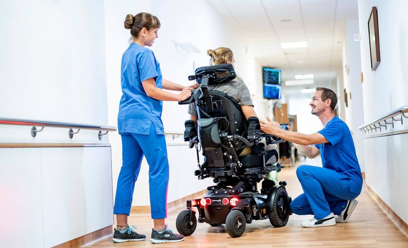 Zwei Pflegekräfte kümmern sich um einen Patienten im Rollstuhl