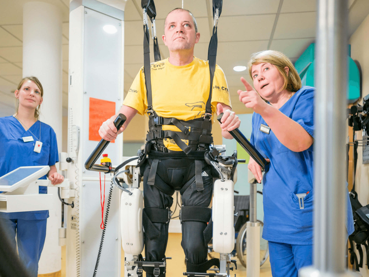 Therapeuten unterstützen Patientin beim Gehenlernen im Gangtrainer