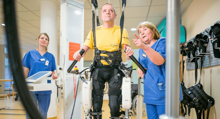 bewegungstherapie Therapeuten unterstützen Patientin beim Gehenlernen im Gangtrainer