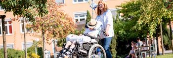 Pflegekraft scheibt Patientin im Rollstuhl im Park um das Krankenhaus Plau am See