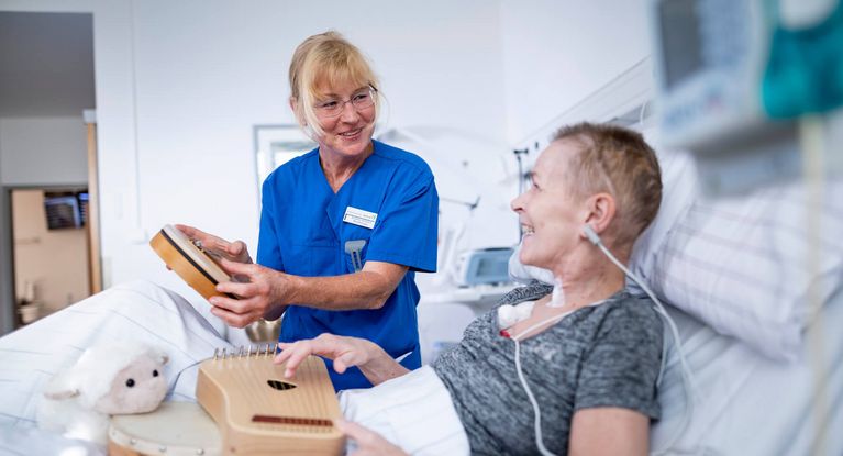Pflegekraft und neurologische Patientin spielen auf kleinen Handtrommeln