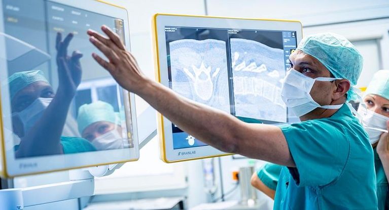 Arzt mit Haube und Mundschutz überwacht Operation an der Wirbelsäule am Bildschirm