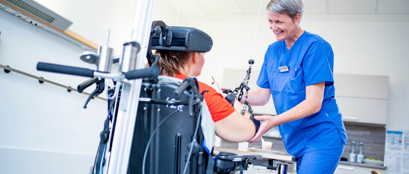 Therapeutin unterstützt Patientin im Rollstuhl bei der Bewegungstherapie